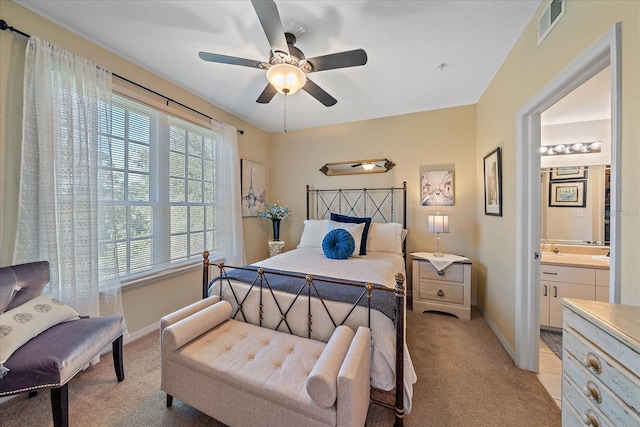 bedroom with light carpet, ensuite bath, multiple windows, and ceiling fan