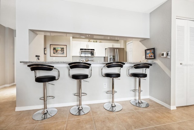 kitchen featuring light stone counters, light tile patterned flooring, a breakfast bar, white cabinets, and appliances with stainless steel finishes