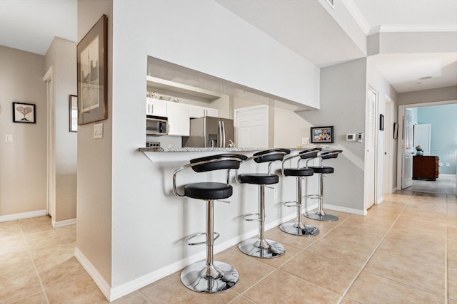 kitchen with kitchen peninsula, a breakfast bar, stainless steel appliances, light tile patterned floors, and white cabinetry