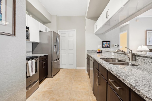 kitchen with dark brown cabinetry, white cabinetry, sink, light stone counters, and appliances with stainless steel finishes