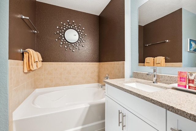 bathroom featuring a bathing tub, vanity, a textured ceiling, and tile walls