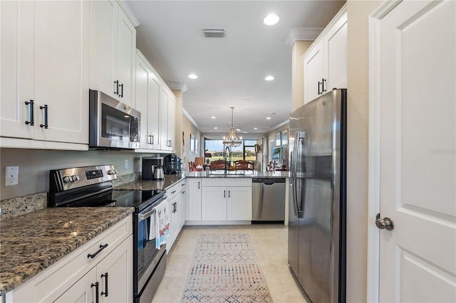 kitchen with appliances with stainless steel finishes, white cabinetry, ornamental molding, and dark stone countertops