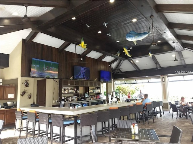 kitchen with beamed ceiling, a breakfast bar, high vaulted ceiling, and wood walls