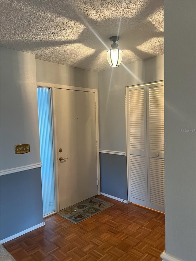 entrance foyer featuring dark parquet floors and a textured ceiling