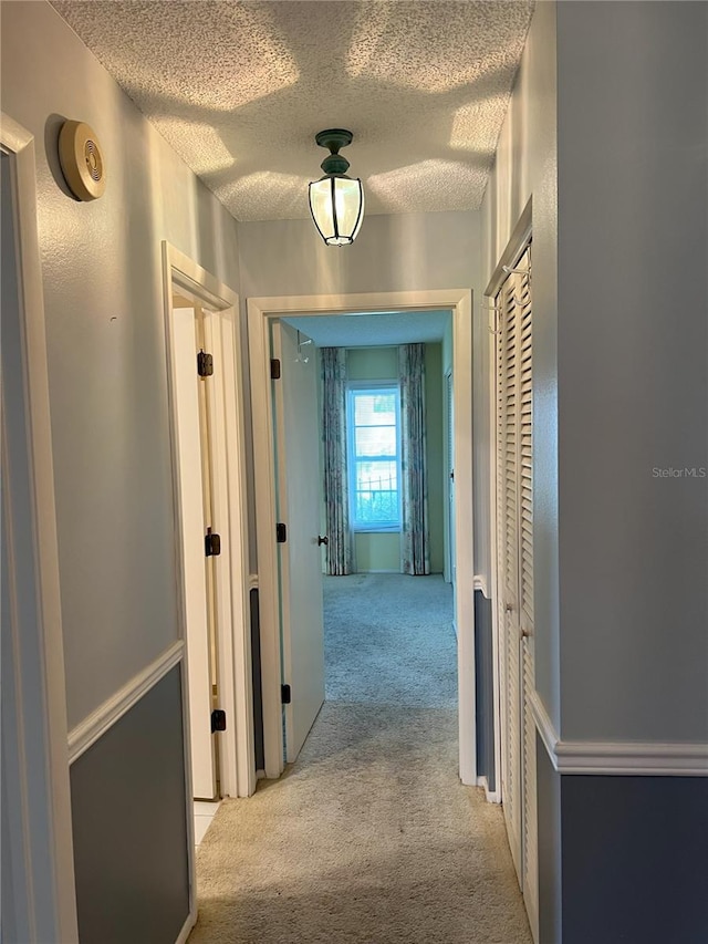 corridor with light colored carpet and a textured ceiling