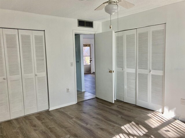 unfurnished bedroom featuring ceiling fan, dark hardwood / wood-style flooring, a textured ceiling, and two closets