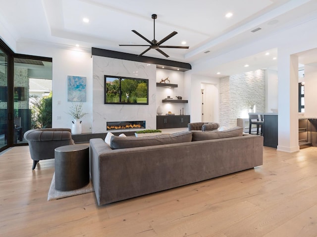 living room with a raised ceiling, ceiling fan, a fireplace, and light hardwood / wood-style floors