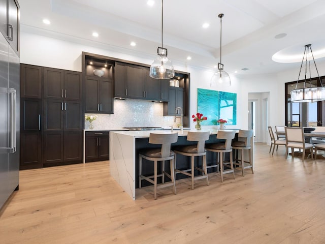 kitchen with a raised ceiling, a center island with sink, decorative light fixtures, and light wood-type flooring