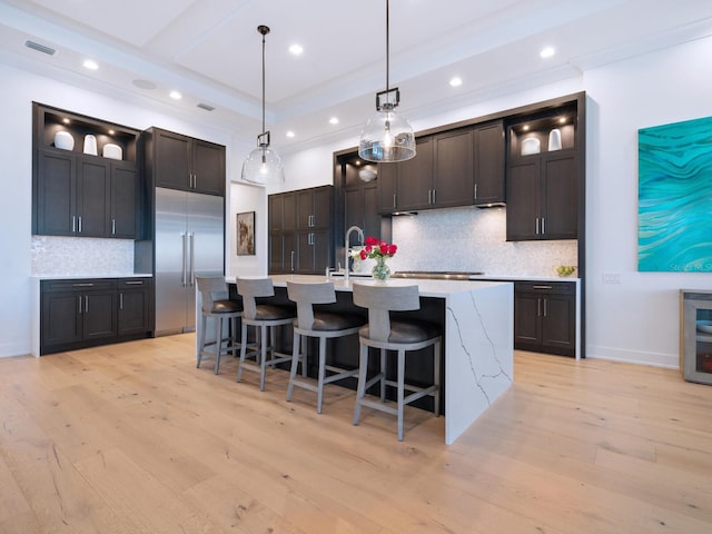 kitchen featuring backsplash, a kitchen island with sink, pendant lighting, light hardwood / wood-style flooring, and stainless steel built in fridge