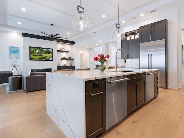 kitchen featuring a center island with sink, hanging light fixtures, sink, appliances with stainless steel finishes, and light hardwood / wood-style floors