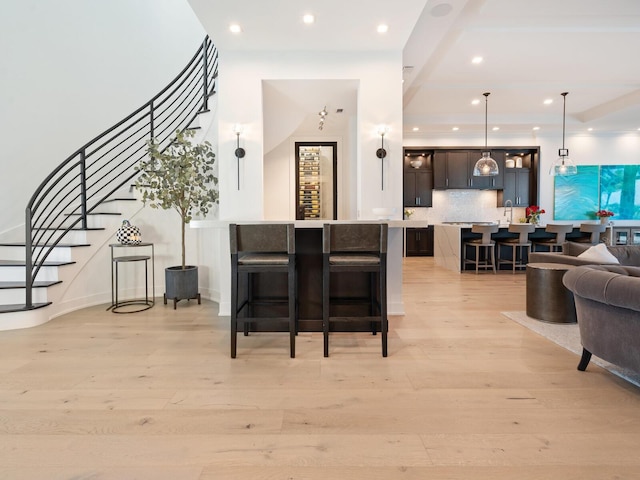 bar with pendant lighting, decorative backsplash, dark brown cabinetry, and light hardwood / wood-style flooring