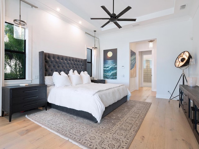 bedroom featuring ceiling fan, light hardwood / wood-style floors, a raised ceiling, and ensuite bath