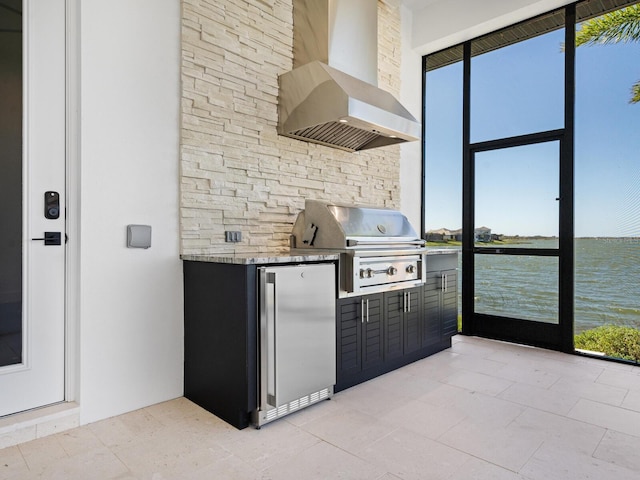 kitchen with a water view, stainless steel refrigerator, plenty of natural light, and wall chimney range hood