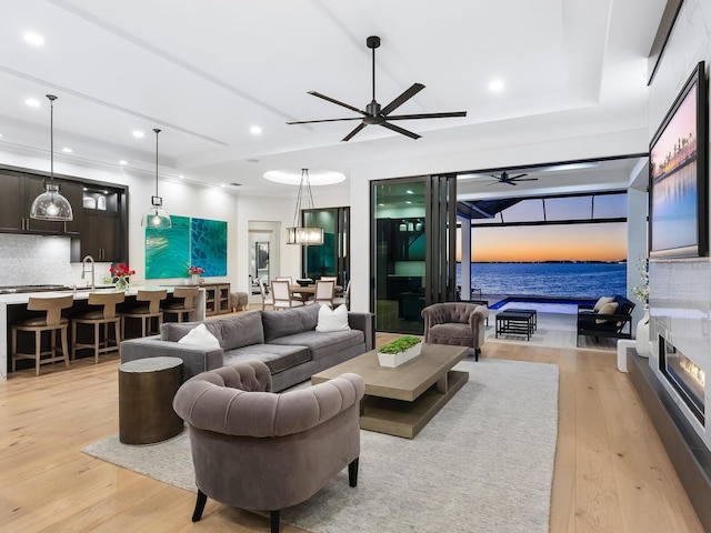 living room with ceiling fan, a water view, sink, and light hardwood / wood-style flooring