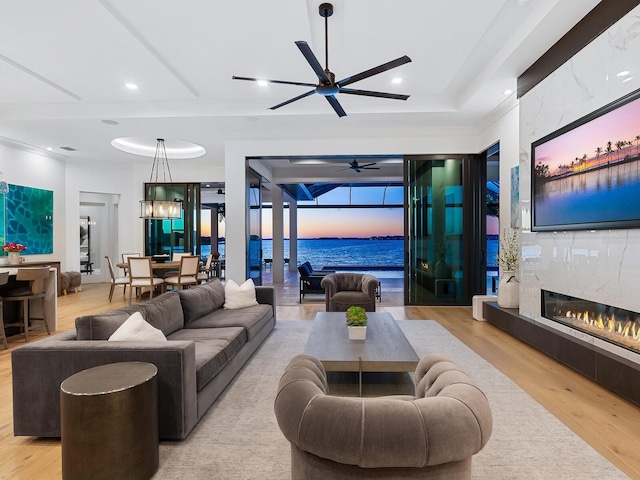 living room featuring a high end fireplace, light hardwood / wood-style floors, a raised ceiling, and ceiling fan