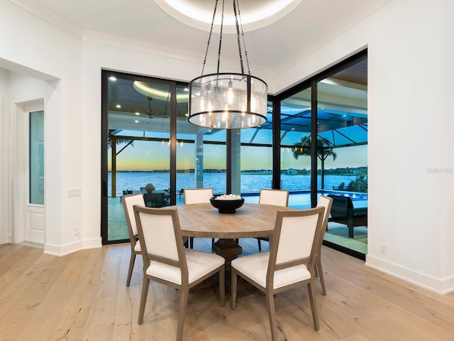 dining area with a chandelier, a water view, light hardwood / wood-style flooring, and ornamental molding