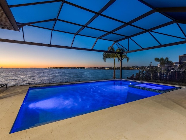 pool at dusk featuring a lanai, a patio area, an in ground hot tub, and a water view