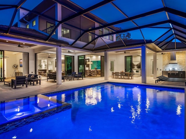 view of pool with glass enclosure, an outdoor hangout area, ceiling fan, exterior kitchen, and a patio