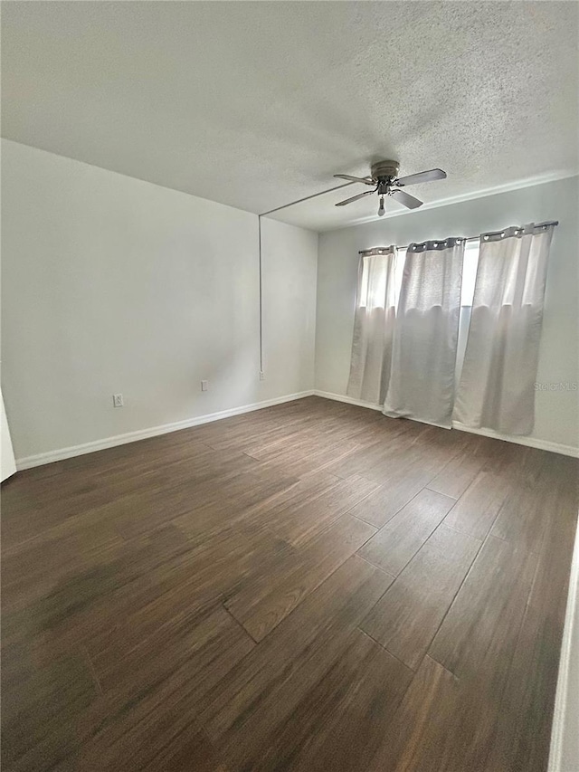 empty room with dark wood finished floors, a textured ceiling, baseboards, and ceiling fan