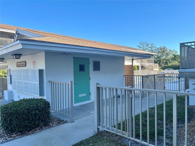 view of side of home with roof with shingles, fence, mail area, and stucco siding