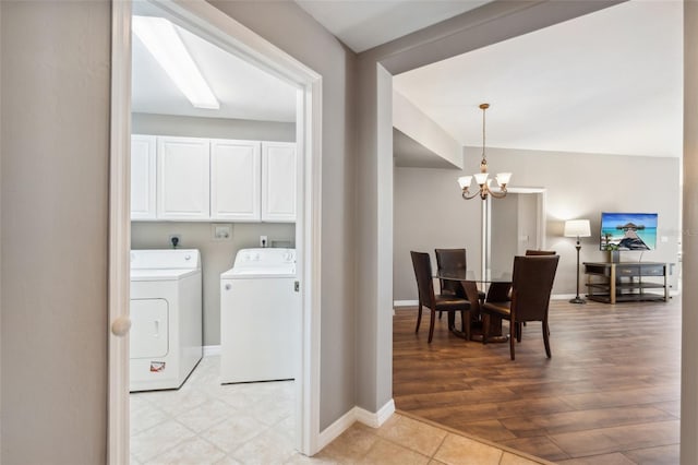 clothes washing area with washer and clothes dryer, a notable chandelier, cabinets, and light hardwood / wood-style flooring