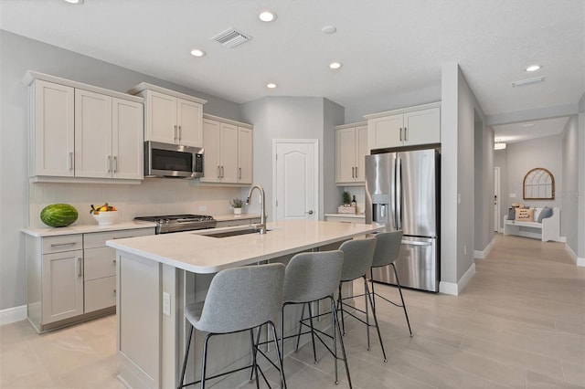 kitchen featuring sink, stainless steel appliances, a kitchen island with sink, and a breakfast bar area