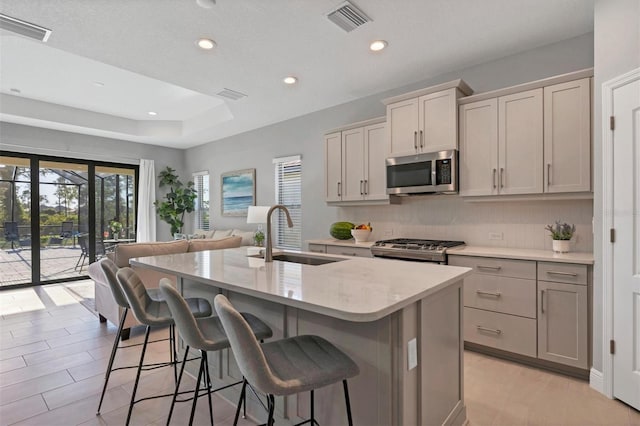 kitchen with gray cabinetry, light stone countertops, sink, a center island with sink, and appliances with stainless steel finishes