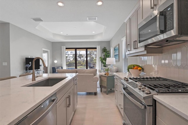 kitchen with light stone countertops, tasteful backsplash, stainless steel appliances, a raised ceiling, and sink