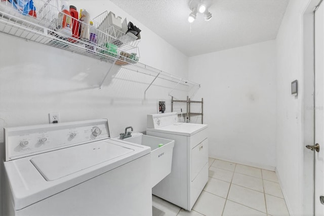 clothes washing area featuring light tile patterned floors, a textured ceiling, and washing machine and clothes dryer