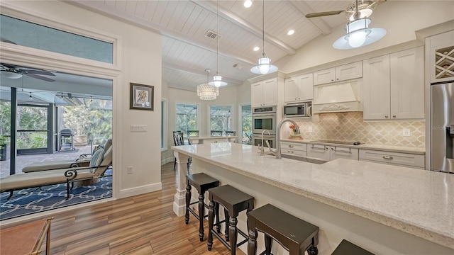 kitchen featuring light stone countertops, wood ceiling, custom range hood, stainless steel appliances, and lofted ceiling with beams