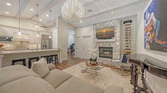 living room featuring wooden ceiling, vaulted ceiling with beams, light hardwood / wood-style floors, a fireplace, and ceiling fan with notable chandelier