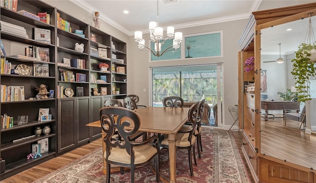 dining space featuring wood-type flooring, ceiling fan with notable chandelier, and crown molding