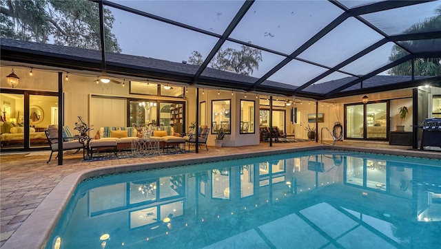 pool at dusk featuring glass enclosure, ceiling fan, a patio area, and an outdoor hangout area