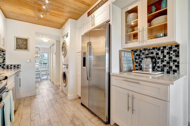 kitchen featuring stainless steel fridge, light stone counters, wood ceiling, stacked washer / dryer, and white cabinets