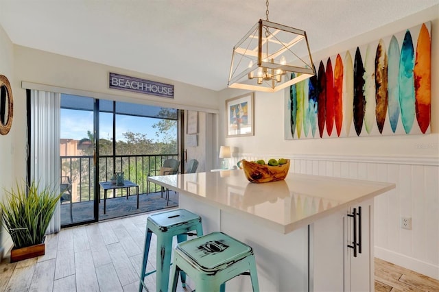 kitchen featuring an inviting chandelier, white cabinets, hanging light fixtures, light hardwood / wood-style floors, and a breakfast bar area