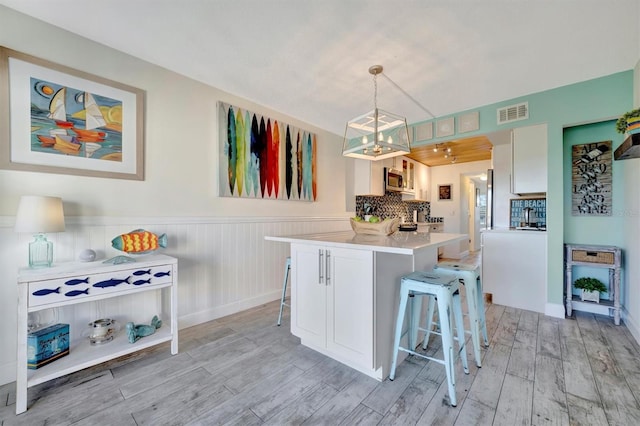 kitchen with pendant lighting, light hardwood / wood-style floors, kitchen peninsula, and a breakfast bar area