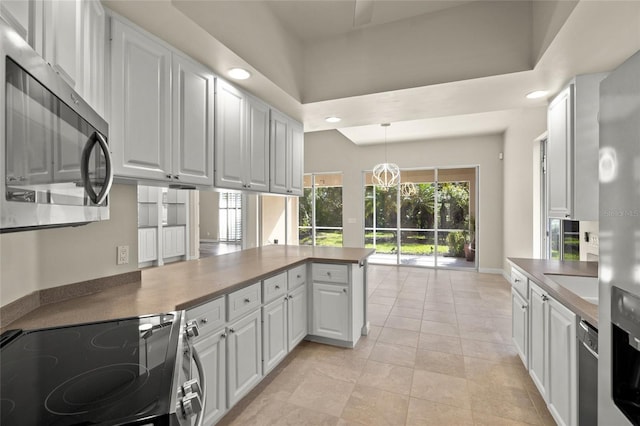 kitchen featuring kitchen peninsula, appliances with stainless steel finishes, white cabinetry, and hanging light fixtures