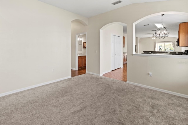 empty room featuring carpet, lofted ceiling, sink, and an inviting chandelier