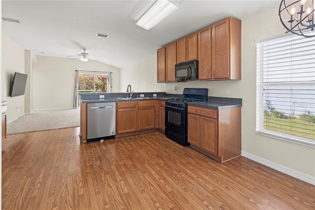 kitchen featuring hanging light fixtures, kitchen peninsula, vaulted ceiling, black appliances, and ceiling fan with notable chandelier