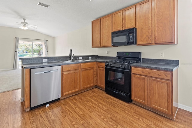 kitchen featuring kitchen peninsula, vaulted ceiling, sink, black appliances, and light hardwood / wood-style floors