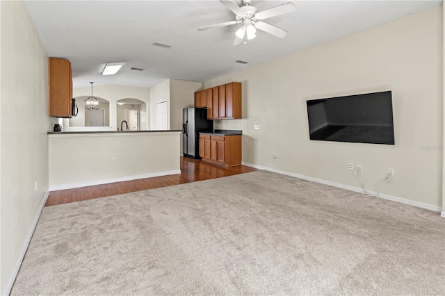 unfurnished living room featuring ceiling fan with notable chandelier, sink, and dark wood-type flooring