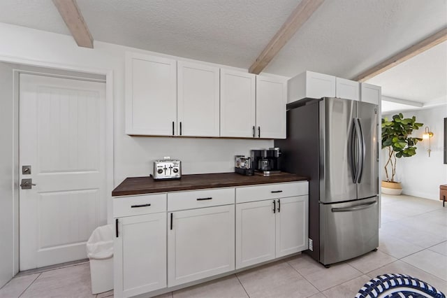 kitchen featuring wooden counters, stainless steel fridge, a textured ceiling, beam ceiling, and white cabinetry