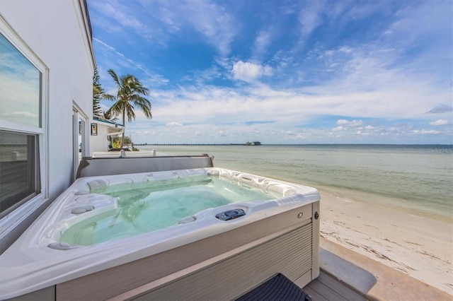 exterior space with a water view, a hot tub, and a beach view