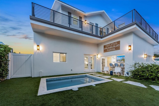 back house at dusk featuring a balcony, a yard, a patio, and french doors