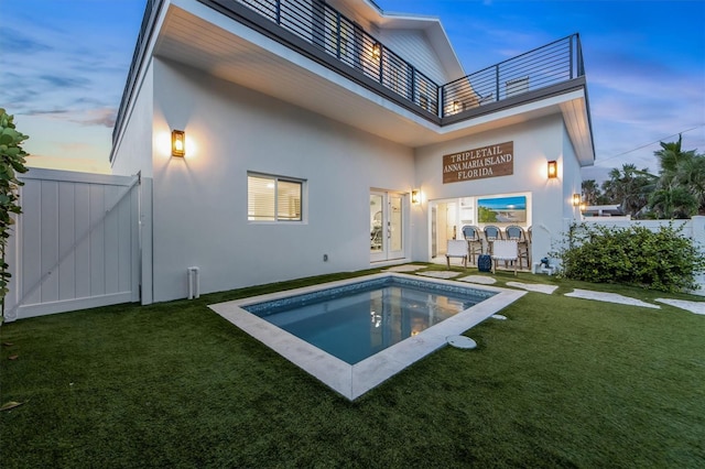 back house at dusk with a lawn, a balcony, and french doors