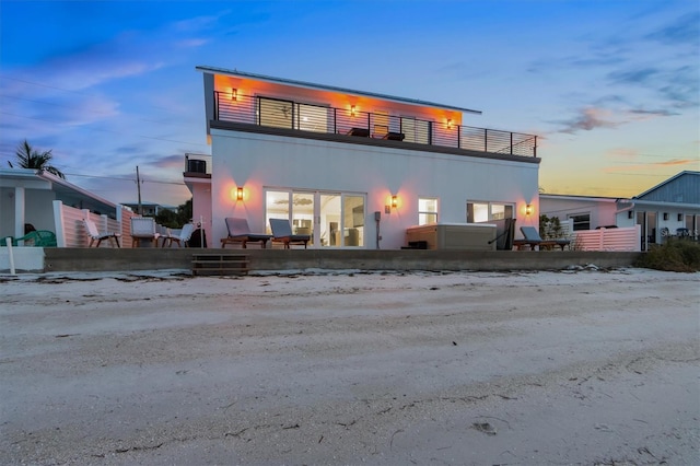 back house at dusk with a jacuzzi and a balcony