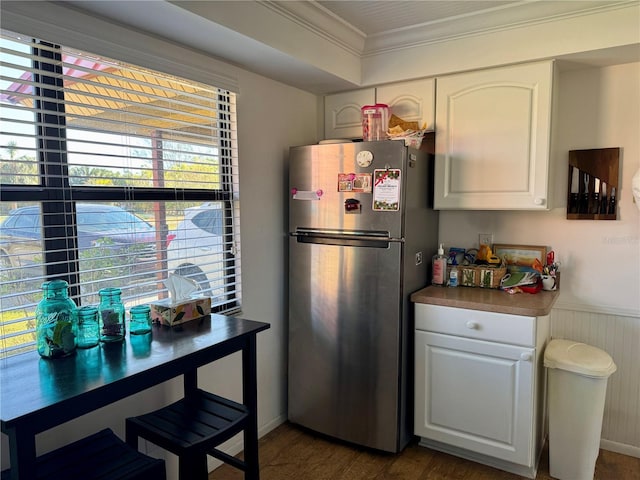 kitchen with ornamental molding, white cabinets, dark hardwood / wood-style floors, stainless steel refrigerator, and wood walls