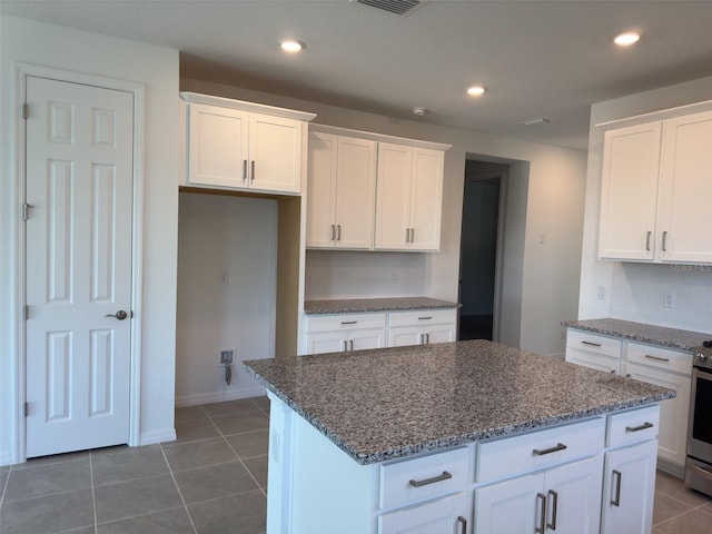 kitchen featuring a kitchen island, stainless steel range with electric cooktop, dark stone counters, white cabinets, and dark tile patterned flooring