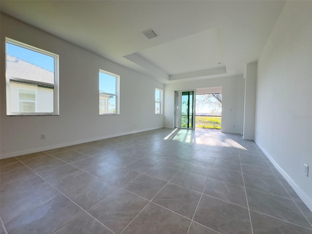 tiled empty room featuring a tray ceiling and plenty of natural light