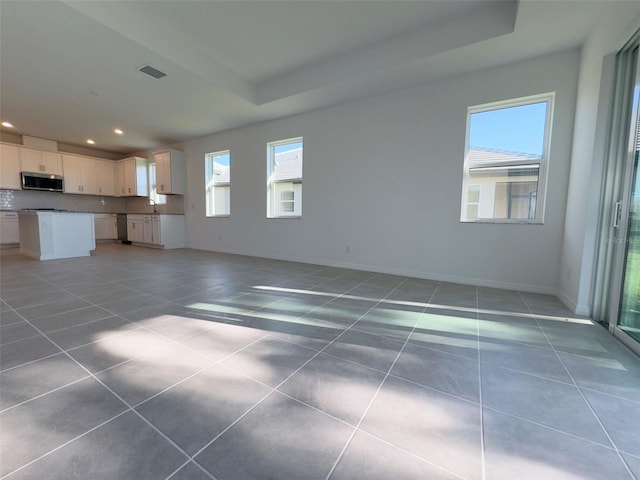 unfurnished living room featuring a tray ceiling, tile patterned floors, and sink